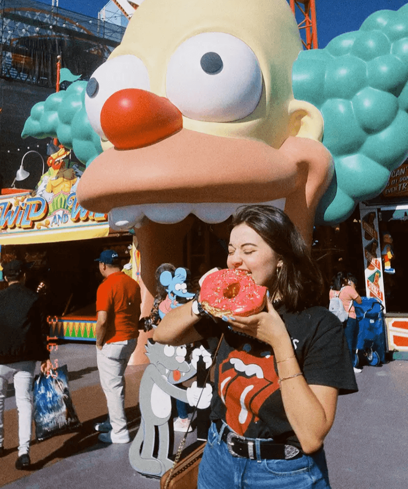 Image of a student eating a giant donut in front of a Krusty the Clown statue, typical of a theme park in the USA during a study programme in the USA.