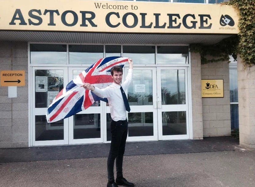 A student holding the British flag in front of a college, ready for an exchange experience in the US, blending education and culture.